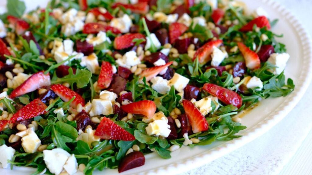 A plate of arugula salad topped with strawberries, feta cheese, nuts, and a light drizzle of dressing.