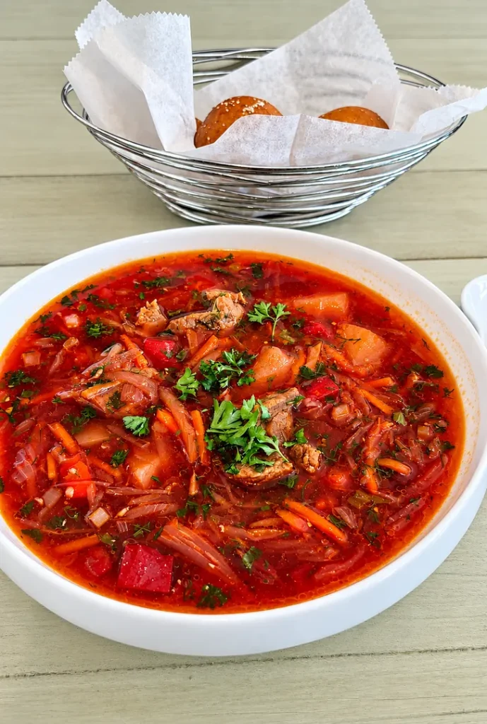 Borsh soup garnished with herbs and served with bread.