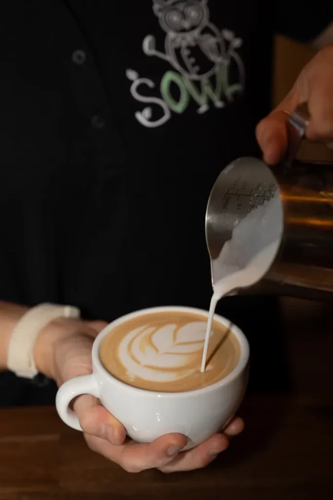 A Sowa barista pouring latte art into a cup of coffee.