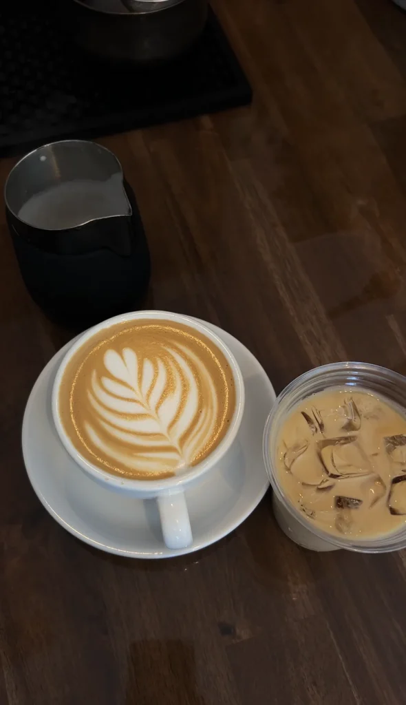 Latte with leaf-shaped foam art beside an iced coffee on a dark wooden table.